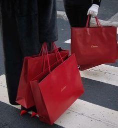 two people carrying red shopping bags on the street with their feet in the air and one person wearing white gloves