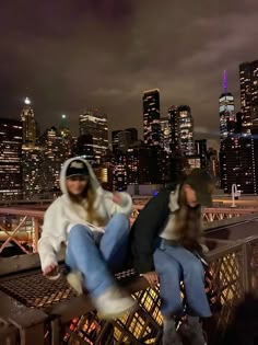 two people sitting on top of a bridge in front of the city skyline at night