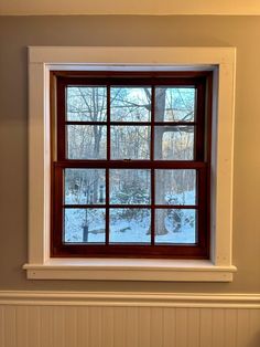 a window in the corner of a room with snow on the ground and trees outside