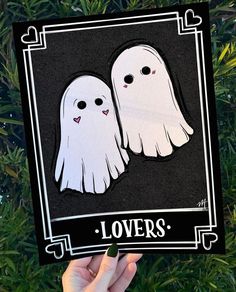 someone holding up a card with two ghost faces in front of some green plants and trees