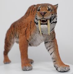 a toy tiger with it's mouth open on a white surface, showing its teeth