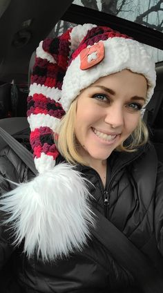 a woman in a car wearing a knitted hat with fur pom - poms