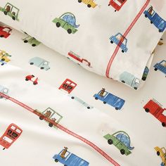 a close up of a bed sheet with cars and trucks on it in the background