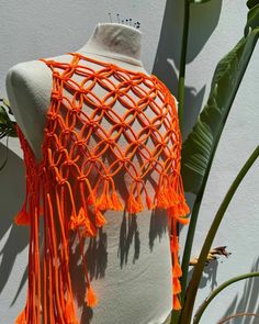 an orange crochet shawl with tassels hanging from it's back