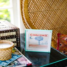 a glass table topped with books next to a wicker basket filled with books and a candle