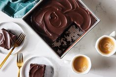 two plates with slices of chocolate cake on them next to cups of coffee and spoons