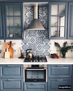 a kitchen with blue cabinets and white counter tops, an oven hood over the stove