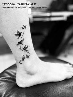 a black and white photo of a tattoo on the foot with birds flying around it