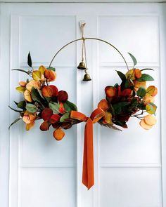 a wreath with orange and yellow flowers hanging on a white door, decorated with an orange ribbon