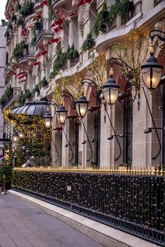 christmas lights are hanging on the side of a building near a fence and lampposts