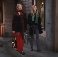 two women are standing on the sidewalk in front of a building and one is holding a handbag