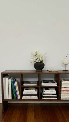 a vase with flowers on top of a wooden shelf next to a bookcase filled with books