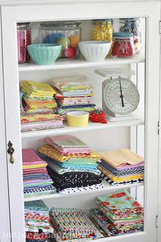 a white bookcase filled with lots of colorful fabrics and quilting material on top of it