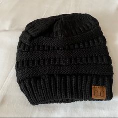 a black knitted beanie with a button on the front and side, sitting on a gray surface