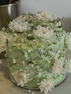 a green cake with white flowers on it sitting on a table next to a pot