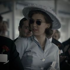 a woman in a hat and sunglasses standing next to other people