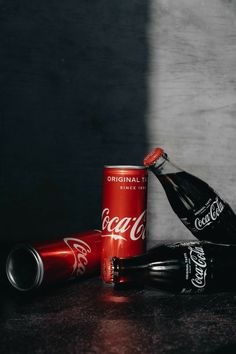 two coca - cola cans and one empty coke can on a table