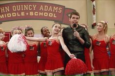 a man standing in front of a group of cheerleaders while holding a microphone