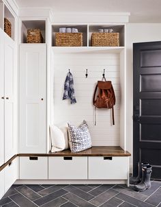 an entryway with white cabinets, black doors and two coats hanging on the wall