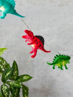 three toy dinosaurs are hanging from strings next to a potted plant with green leaves