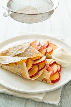 a white plate topped with fruit covered in pastry next to a bowl of yogurt