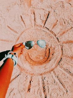 a person wearing sunglasses standing in the sand with their hand on top of each other