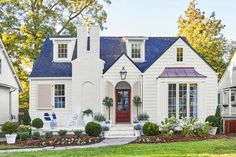 a white house with blue shingles and red shutters on the front door is shown