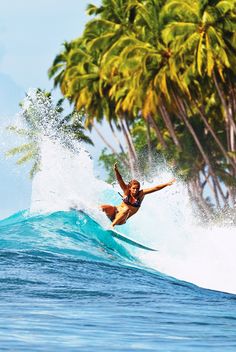 a man riding a wave on top of a surfboard in front of palm trees