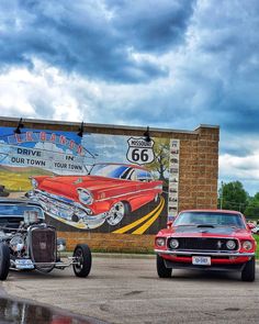 two cars parked in front of a building with a mural on the wall behind them