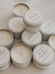 six white candles sitting on top of each other next to each other in small tins