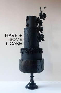 a three tiered cake with black icing and flowers on the top is displayed against a white background