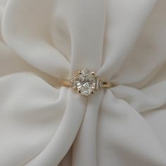 a diamond ring sitting on top of a white satin material with a flower in the middle