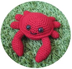 a red crocheted crab laying on top of green carpet