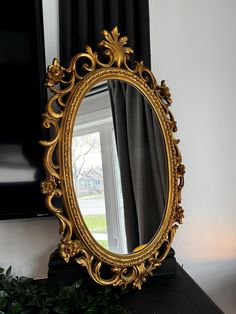 an ornate gold framed mirror sitting on top of a black table next to a window