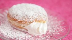 a powdered doughnut with icing on a pink tablecloth covered glass plate