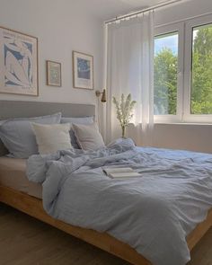 a bed with blue sheets and pillows in a bedroom next to two large windows on the wall