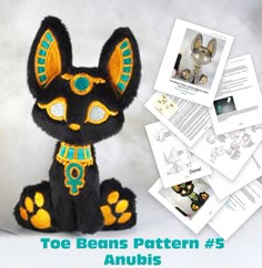 a black and yellow stuffed animal sitting on top of a pile of white papers with the words toe beans pattern 5 anubis written below it