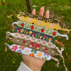 a hand holding five different colored bracelets in it's palm, with trees and grass in the background