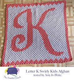 a red and white crocheted afghan with the letter k on it's side