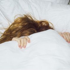 a woman is laying in bed with her head on the pillow and she has long hair