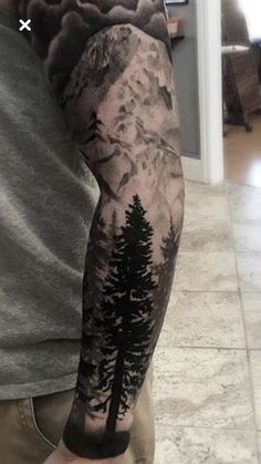 a man's arm with trees and mountains on it