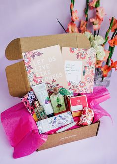 a box filled with lots of different items on top of a pink table cloth next to flowers