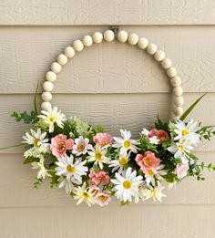 a white beaded wreath with pink and yellow flowers hanging on the side of a house