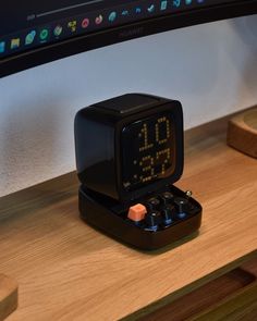 an alarm clock sitting on top of a wooden desk next to a computer monitor and keyboard