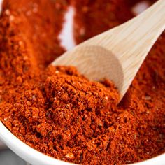 a wooden spoon in a white bowl filled with red chili powder and seasoning flakes