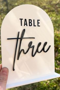 a hand holding up a sign that says table three