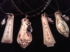 four silver necklaces with words on them hanging from a black cord in front of a black background