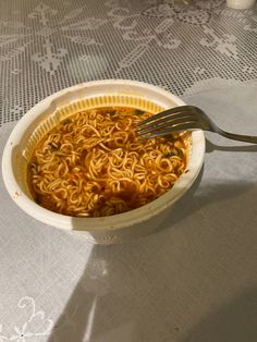 a bowl of noodles is sitting on a table with a fork and spoon in it