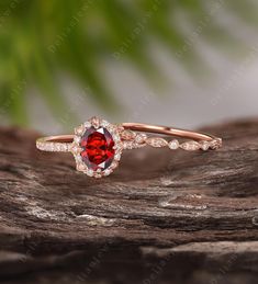 a red stone ring sitting on top of a piece of wood with leaves in the background