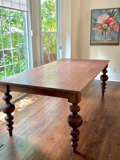 a large wooden table sitting in the middle of a living room next to two windows